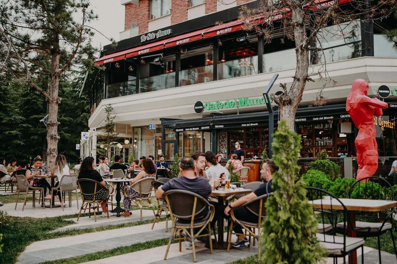 People enjoying a casual gathering at an outdoor cafe, surrounded by greenery and city atmosphere.